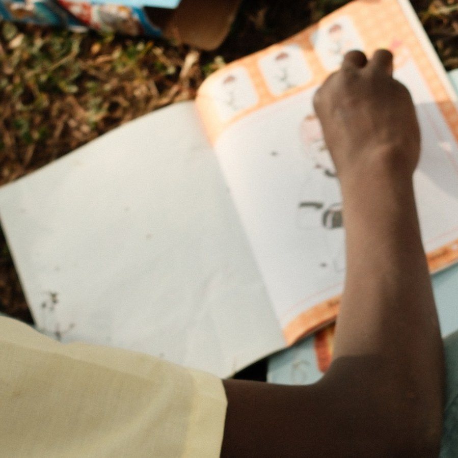 A child coloring in a workbook during an outdoor session, seen from behind