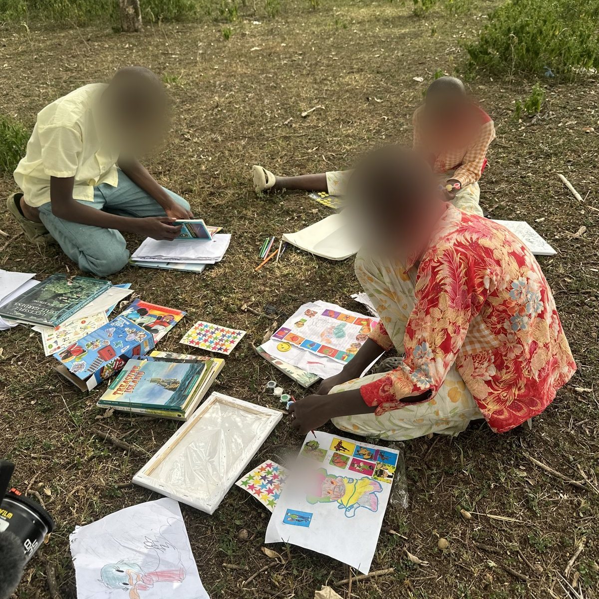 Children drawing and painting outdoors in Kenya, faces blurred for privacy